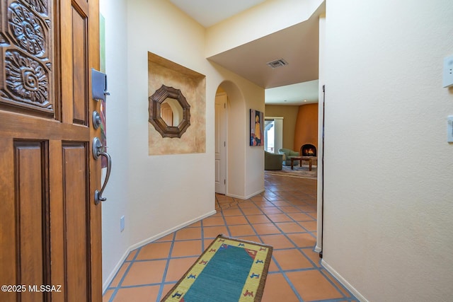 corridor featuring visible vents, arched walkways, baseboards, and light tile patterned flooring