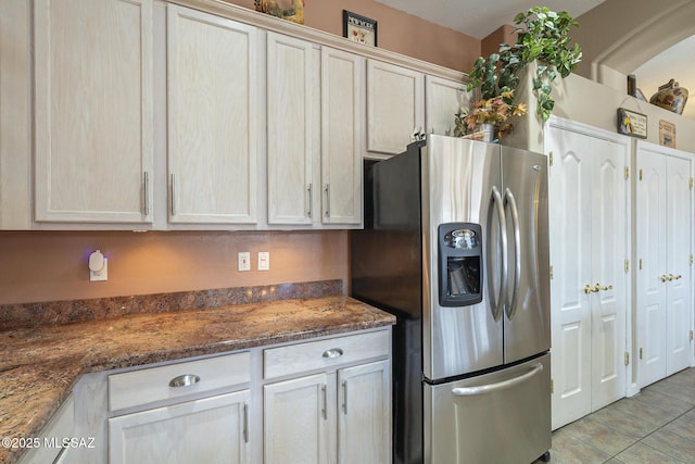 kitchen with stainless steel fridge, light tile patterned floors, and dark stone countertops