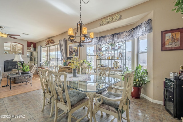 tiled dining space with ceiling fan with notable chandelier, a fireplace, and beverage cooler