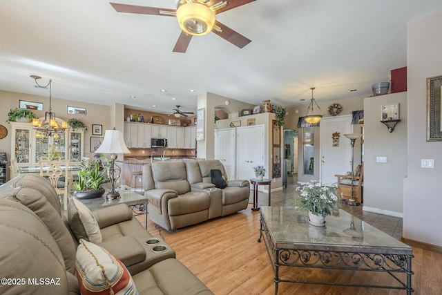 living room with ceiling fan with notable chandelier and light hardwood / wood-style flooring