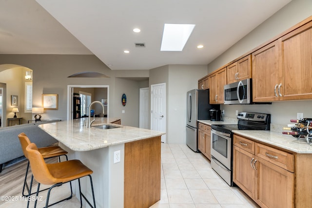 kitchen with a breakfast bar area, light stone countertops, an island with sink, a sink, and stainless steel appliances