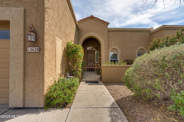 view of exterior entry with a tile roof, a gate, and stucco siding