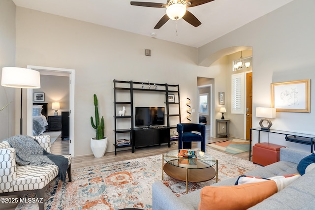 living area featuring arched walkways, a high ceiling, wood finished floors, and ceiling fan with notable chandelier