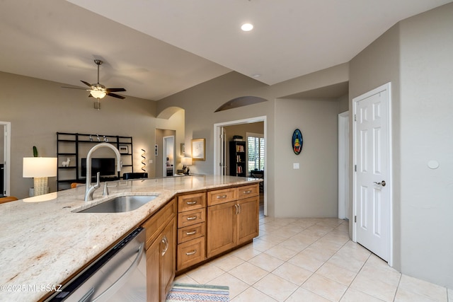 kitchen with a sink, ceiling fan, light stone countertops, brown cabinets, and stainless steel dishwasher