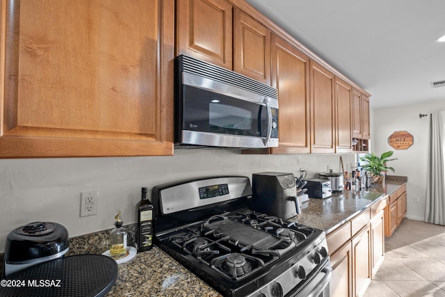 kitchen featuring appliances with stainless steel finishes, light tile patterned floors, and dark stone countertops