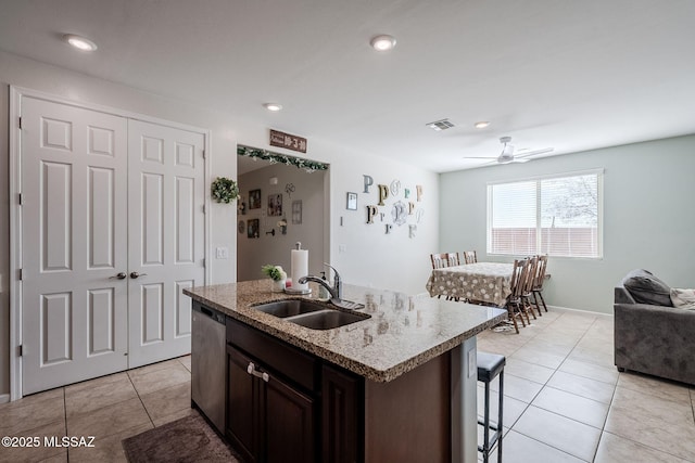 kitchen featuring an island with sink, sink, a breakfast bar area, stainless steel dishwasher, and dark brown cabinets