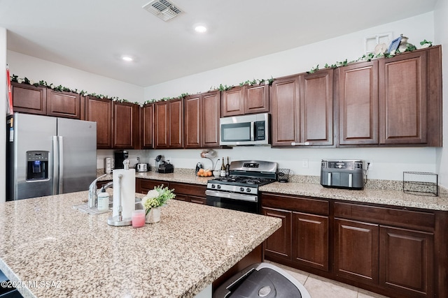 kitchen with light stone counters, a kitchen island with sink, stainless steel appliances, and light tile patterned flooring