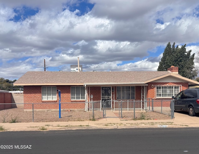 ranch-style home with a fenced front yard, brick siding, and a shingled roof