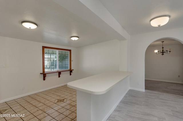 kitchen with a chandelier, arched walkways, a peninsula, and baseboards