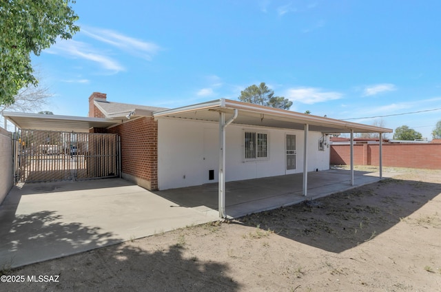 exterior space featuring driveway, a chimney, fence, a carport, and brick siding