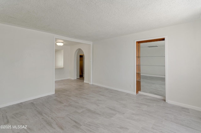 unfurnished room with arched walkways, a textured ceiling, and baseboards