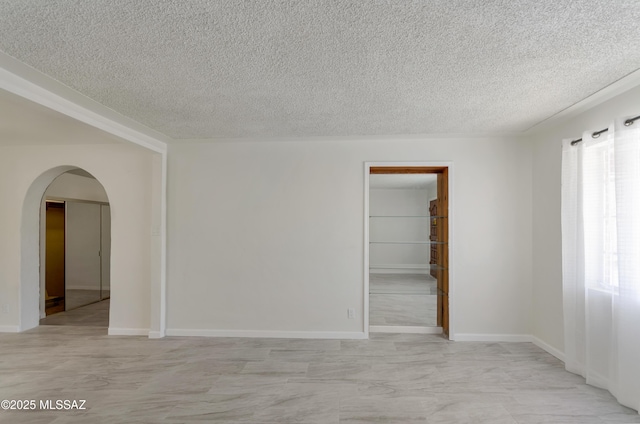 unfurnished room featuring arched walkways, a textured ceiling, and baseboards