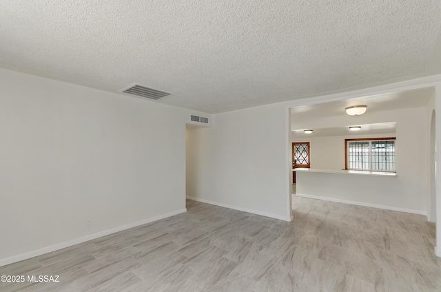 unfurnished room featuring a textured ceiling, wood finished floors, visible vents, and baseboards