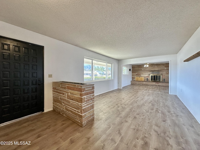 unfurnished living room featuring a textured ceiling, a glass covered fireplace, wood finished floors, and baseboards