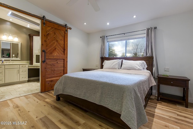 bedroom with visible vents, ensuite bath, lofted ceiling, a barn door, and light wood-type flooring