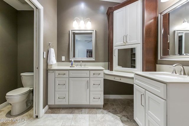 full bath featuring a sink, baseboards, toilet, and two vanities