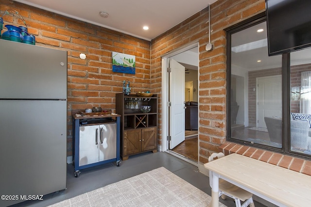 kitchen with brick wall, concrete flooring, and freestanding refrigerator