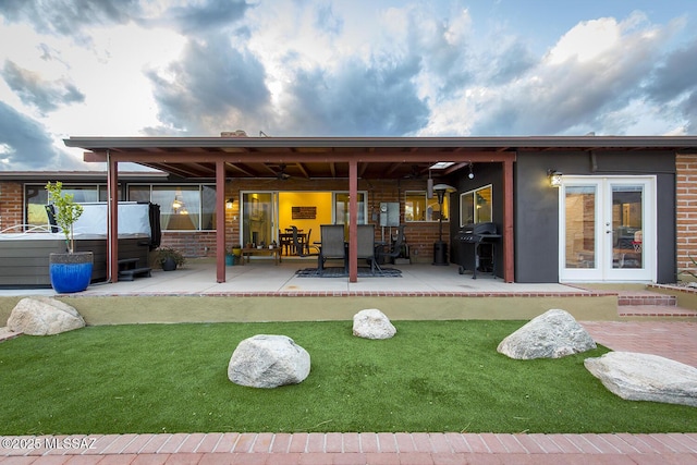 rear view of property featuring french doors, brick siding, a lawn, and a patio area