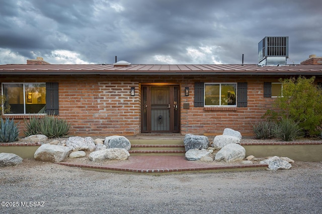 view of front of house featuring metal roof, brick siding, central AC unit, and a chimney