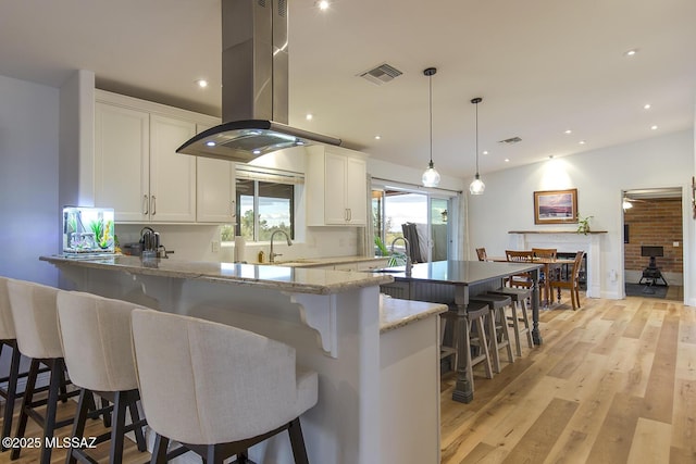 kitchen featuring light wood-style flooring, island exhaust hood, a sink, white cabinetry, and a breakfast bar area