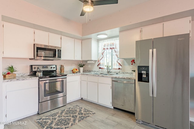 kitchen with a sink, white cabinetry, a ceiling fan, appliances with stainless steel finishes, and light wood finished floors