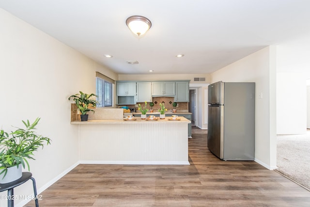 kitchen with decorative backsplash, wood-type flooring, stainless steel fridge, and kitchen peninsula