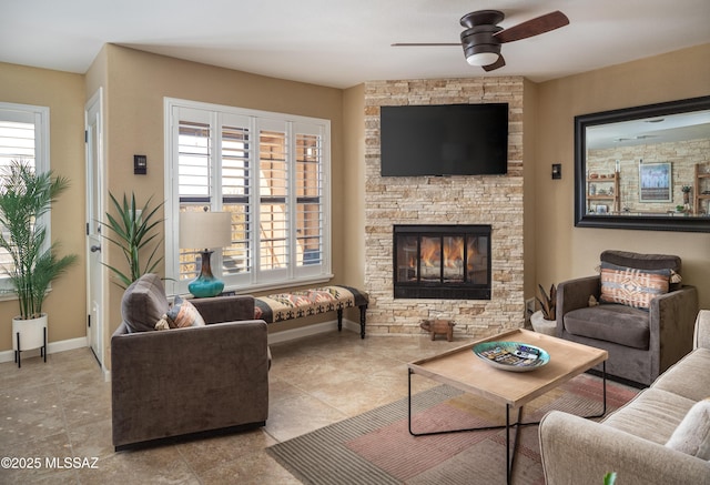 living room featuring ceiling fan, a healthy amount of sunlight, and a stone fireplace