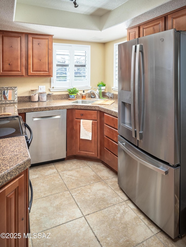 kitchen featuring appliances with stainless steel finishes, sink, light tile patterned floors, a tray ceiling, and a textured ceiling