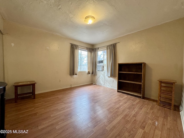 unfurnished room with a textured ceiling, baseboards, and wood finished floors