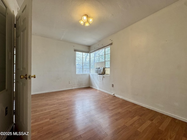 spare room featuring cooling unit, baseboards, and wood finished floors