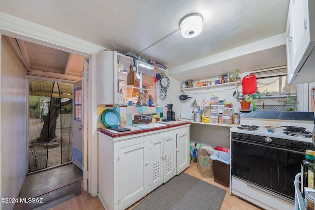 kitchen with white cabinets, tile countertops, gas range oven, open shelves, and a sink