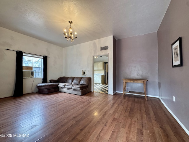 unfurnished living room with baseboards, wood finished floors, visible vents, and an inviting chandelier