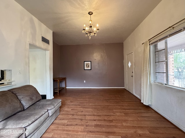 living area with baseboards, a notable chandelier, visible vents, and wood finished floors