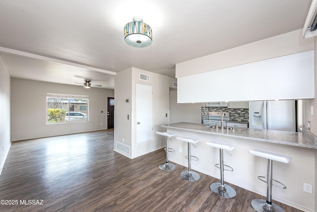 kitchen with visible vents, a sink, dark wood finished floors, white fridge with ice dispenser, and decorative backsplash