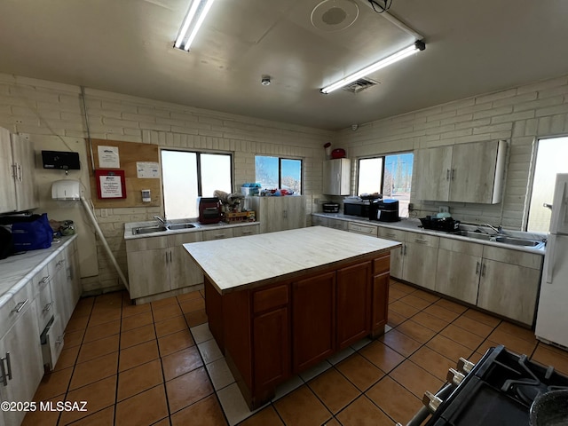 kitchen featuring dark tile patterned floors, a sink, a kitchen island, light countertops, and freestanding refrigerator