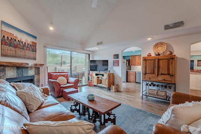 living area with arched walkways, visible vents, light wood-style flooring, and a tile fireplace