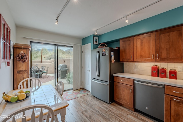 kitchen with stainless steel appliances, brown cabinets, backsplash, and track lighting