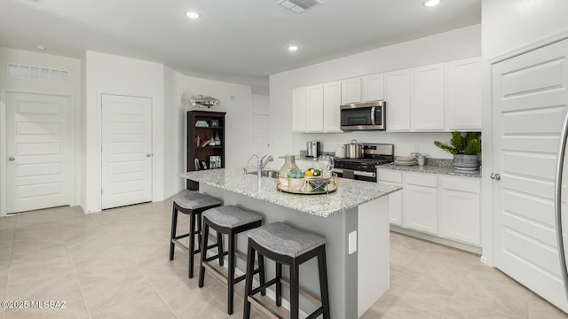 kitchen featuring light stone counters, appliances with stainless steel finishes, a kitchen island with sink, and white cabinets