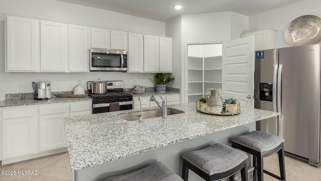 kitchen with sink, light tile patterned floors, appliances with stainless steel finishes, an island with sink, and white cabinets