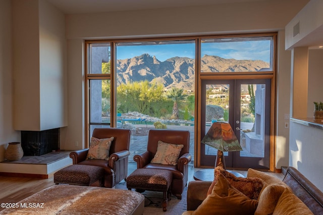 sitting room with a tiled fireplace, wood-type flooring, a mountain view, and french doors