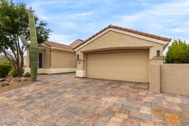 mediterranean / spanish house with decorative driveway, stucco siding, an attached garage, fence, and a tiled roof