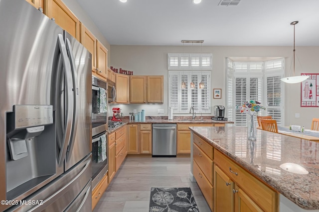 kitchen featuring light wood-style flooring, light stone counters, appliances with stainless steel finishes, pendant lighting, and a sink