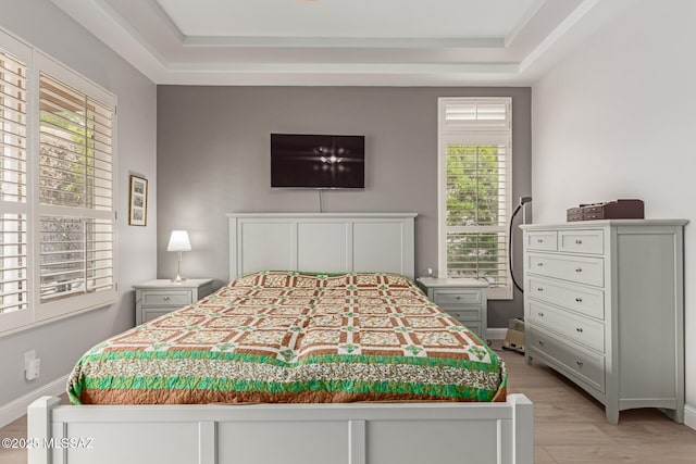 bedroom featuring light wood-type flooring, a tray ceiling, and baseboards