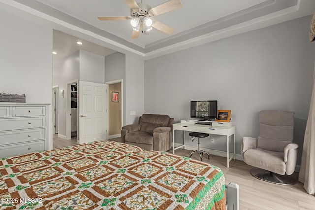 bedroom with baseboards, ceiling fan, a raised ceiling, and light wood-style floors