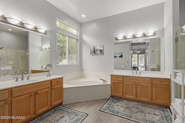 full bathroom featuring wood finished floors, two vanities, a sink, a shower stall, and a bath