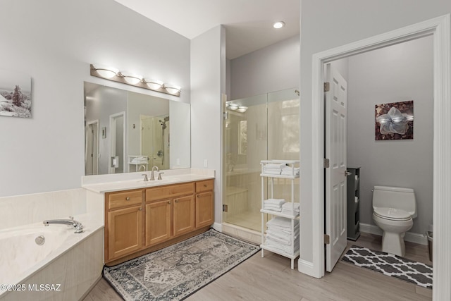 bathroom featuring a stall shower, toilet, wood finished floors, a garden tub, and vanity