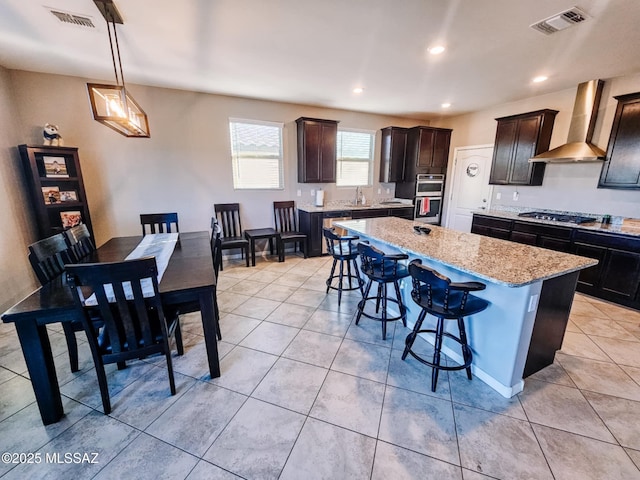 kitchen featuring wall chimney exhaust hood, a breakfast bar area, visible vents, and a center island