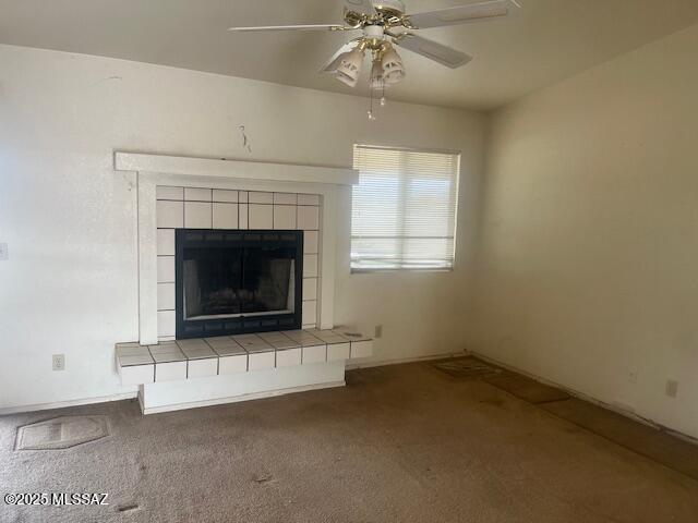 unfurnished living room featuring ceiling fan, a tiled fireplace, and carpet floors