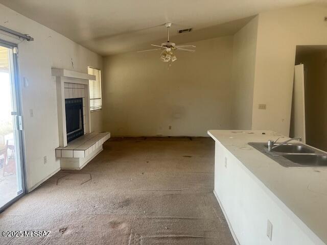 unfurnished living room featuring carpet floors, sink, ceiling fan, and a fireplace