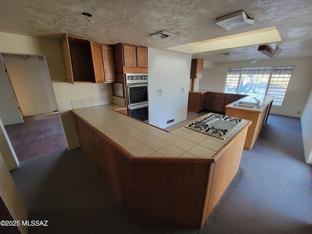 kitchen with stainless steel gas cooktop, tile countertops, a textured ceiling, and kitchen peninsula